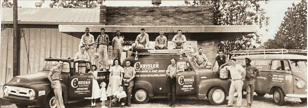 Men, two children, and three industrial service vehicles stand outside a brick building.